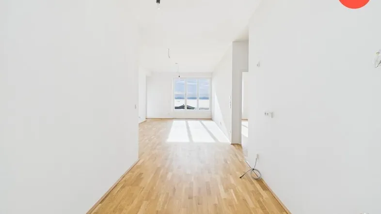 Helles, leeres Wohnzimmer mit Parkettboden und weitem Blick auf die Landschaft.