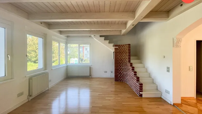 Helles Wohnzimmer mit Holzbalkendecke, Parkettboden und einer markanten Ziegelstein-Treppe.