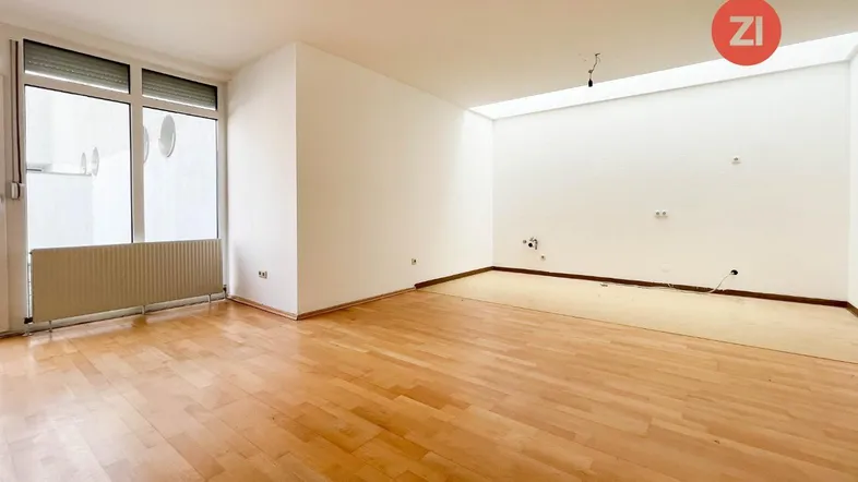 Helles, leeres Zimmer mit Parkettboden und Zugang zu einem Außenbereich durch große Fenster.