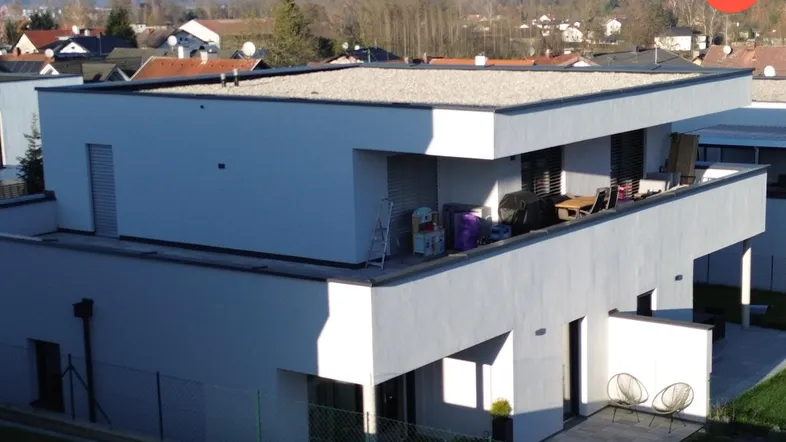 Modernes Gebäude mit Flachdach und großer Terrasse, umgeben von grüner Landschaft.