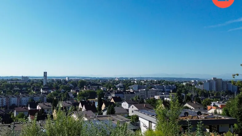 Panoramablick über eine Stadt mit Wohngebäuden und grüner Landschaft im Vordergrund.