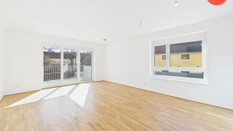 Helles Wohnzimmer mit Parkettboden, großen Fenstern und Zugang zu einem Balkon.