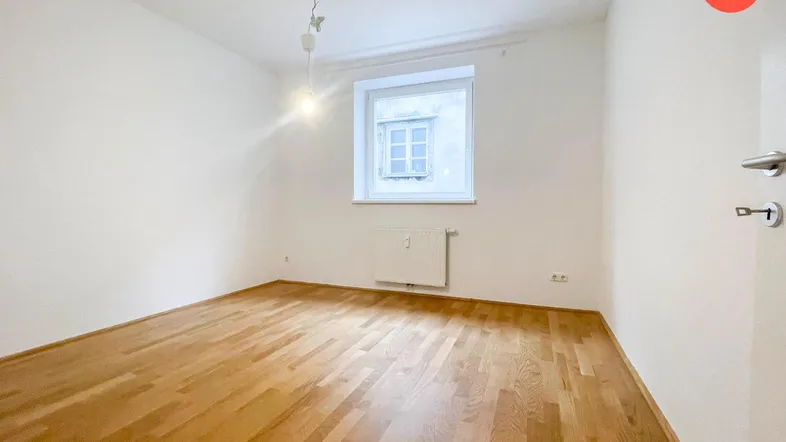 Helles Zimmer mit Parkettboden und weiß gestrichenen Wänden, ideal als Schlaf- oder Wohnbereich.