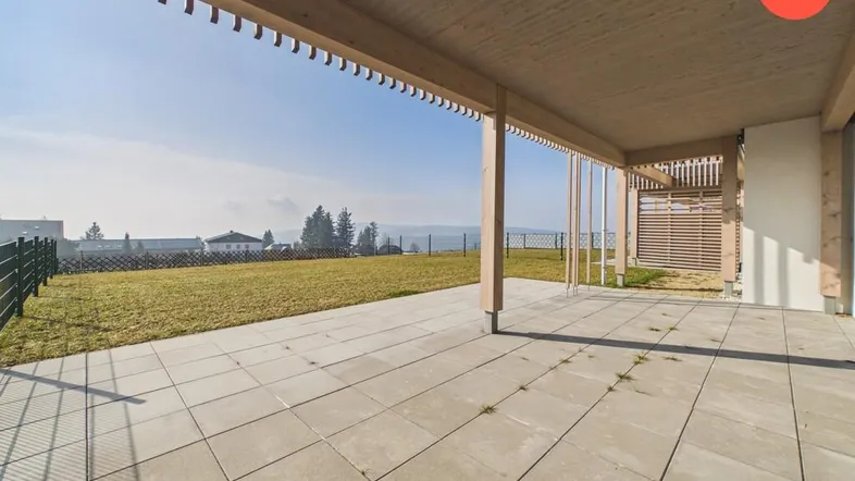 Große gepflasterte Terrasse mit Holzpergola und weitem Blick ins Grüne, ideal für Entspannung.