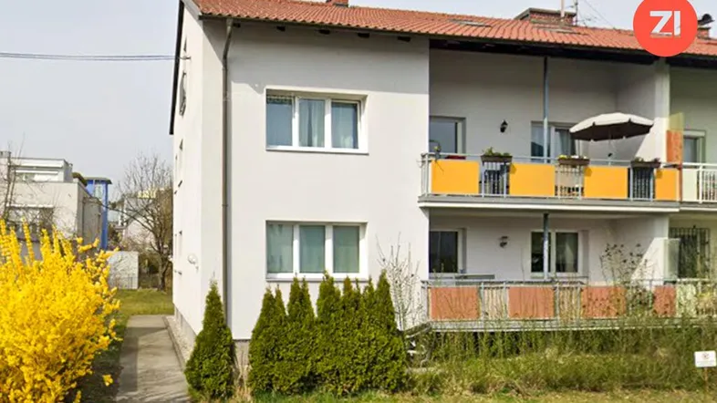 Mehrfamilienhaus mit Balkonen und gepflegtem Vorgarten, umgeben von grüner Vegetation.