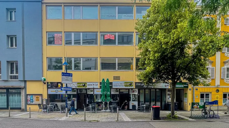 Gelbes Gebäude mit Geschäften im Erdgeschoss und Büros darüber, an einer belebten Straße gelegen.