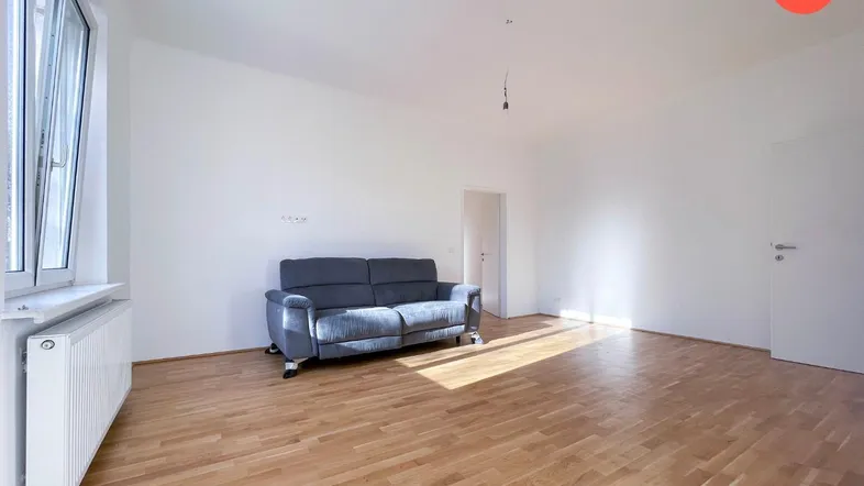 Helles Wohnzimmer mit Parkettboden, einem Sofa und großen Fenstern, die viel Tageslicht hereinlassen.