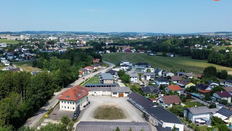 Luftaufnahme des Anwesens mit mehreren Gebäuden, umgeben von Wohnsiedlungen, Feldern und Wäldern unter blauem Himmel.