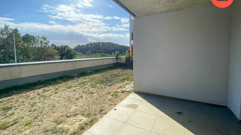 Geflieste Terrasse mit angrenzendem Gartenbereich und Blick ins Grüne unter blauem Himmel.