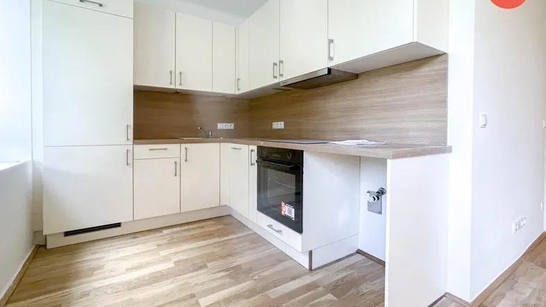 Moderne Einbauküche mit weißen Schränken, integriertem Backofen und hellem Holzfußboden.