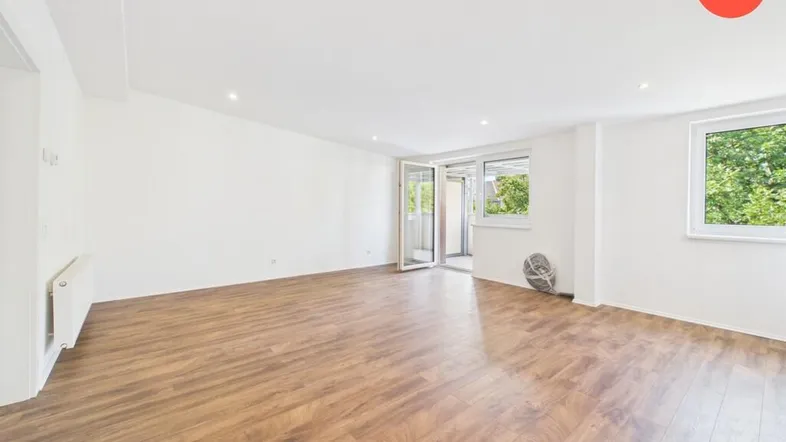 Helles, leeres Wohnzimmer mit Laminatboden und Zugang zu einem Balkon, bereit für die Einrichtung.
