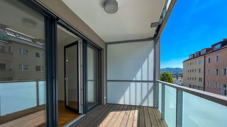 Heller Balkon mit Holzboden, Glasgeländer und weitem Blick über die Stadt.