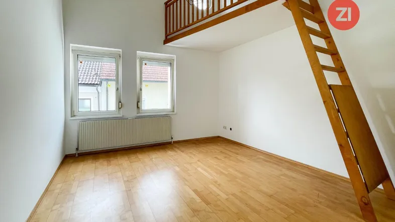 Helles Zimmer mit Holzboden, hohen Decken und einer Holzgalerie mit Leiter.