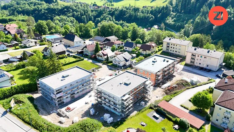 Luftaufnahme einer Wohnsiedlung mit Neubauten im Bau und grüner Umgebung, umgeben von Hügeln.