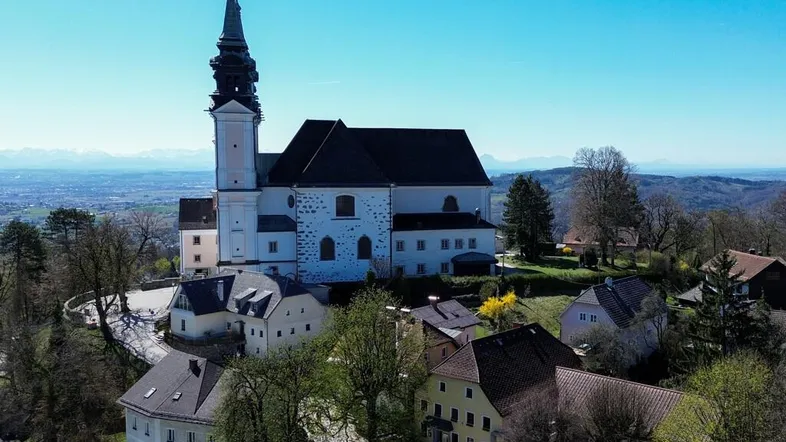 Luftaufnahme einer historischen Kirche mit umliegenden Gebäuden und einer weiten Landschaft im Hintergrund.