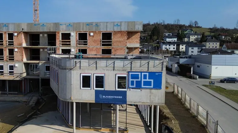 Baustelle eines neuen Gebäudes mit Rohbau, Betonstrukturen und Ziegelwänden unter blauem Himmel.