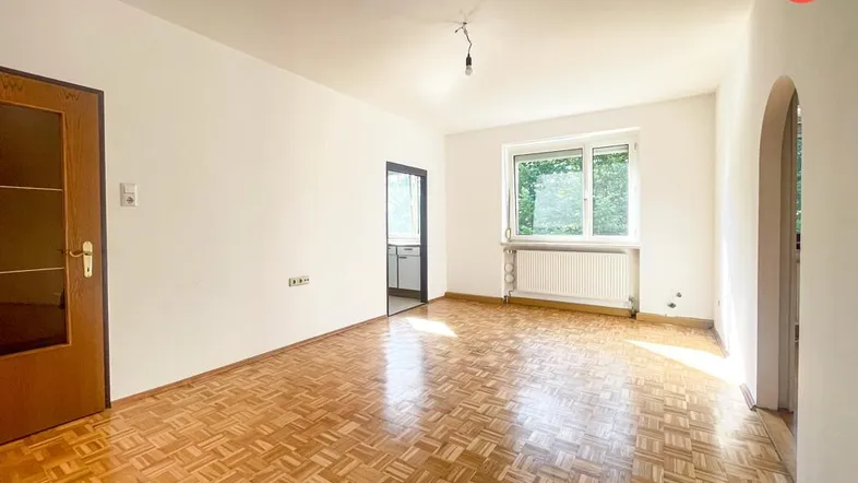 Helles Wohnzimmer mit Parkettboden, weißen Wänden und Fenster mit Blick ins Grüne.
