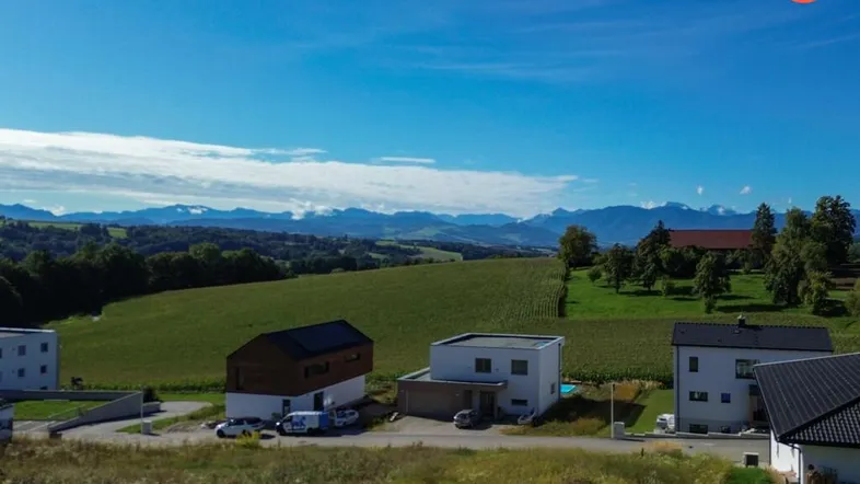 Luftaufnahme einer modernen Wohnsiedlung mit Neubauten, umgeben von grünen Feldern und Bergpanorama.