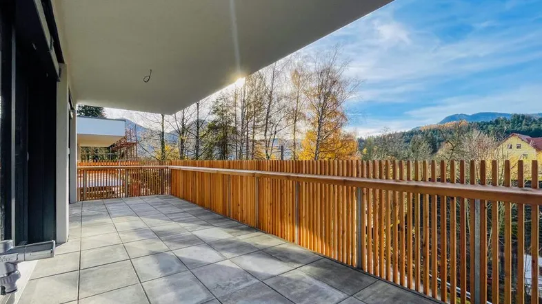 Geräumiger Balkon mit Fliesenboden, Holzgeländer und weitem Blick auf die umliegende Natur und Berge.