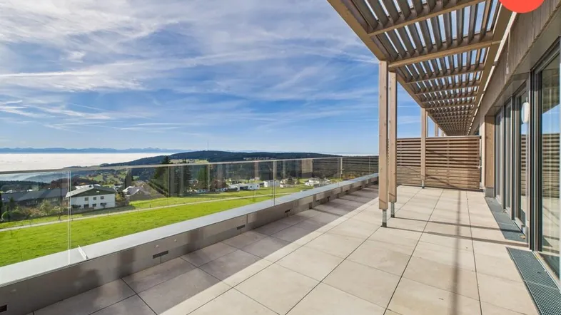 Große Dachterrasse mit Holzdach und Glasgeländer bietet einen weiten Blick über die Landschaft und die Wolken.