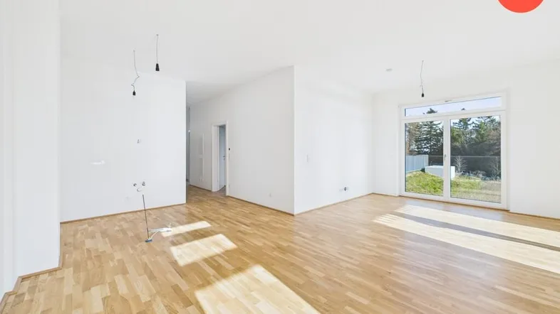 Helles, leeres Wohnzimmer mit Parkettboden und Zugang zu einem Außenbereich.