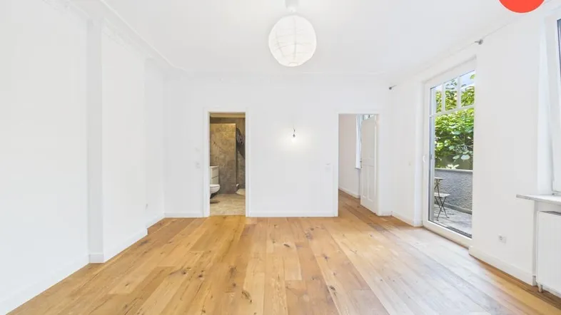 Helles Wohnzimmer mit Holzboden, hohen Decken und Zugang zu einem kleinen Außenbereich.