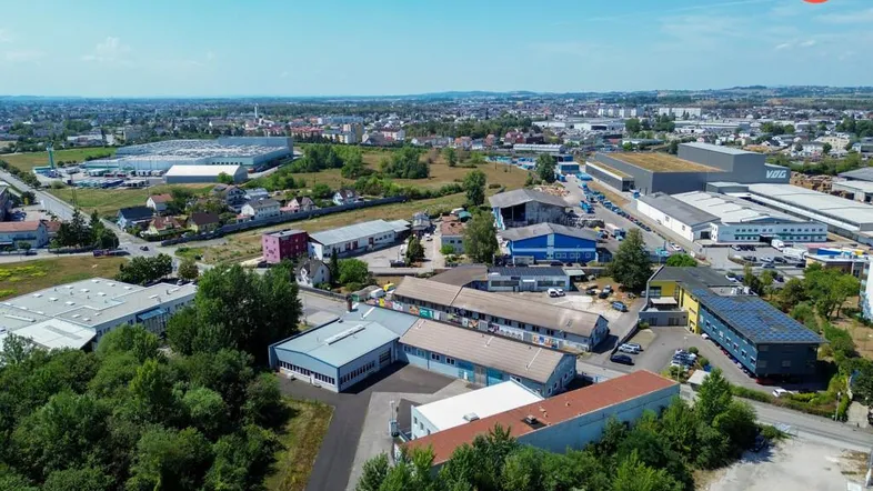 Luftaufnahme eines Gewerbegebiets mit verschiedenen Gebäuden, Straßen und viel Grünfläche unter blauem Himmel.