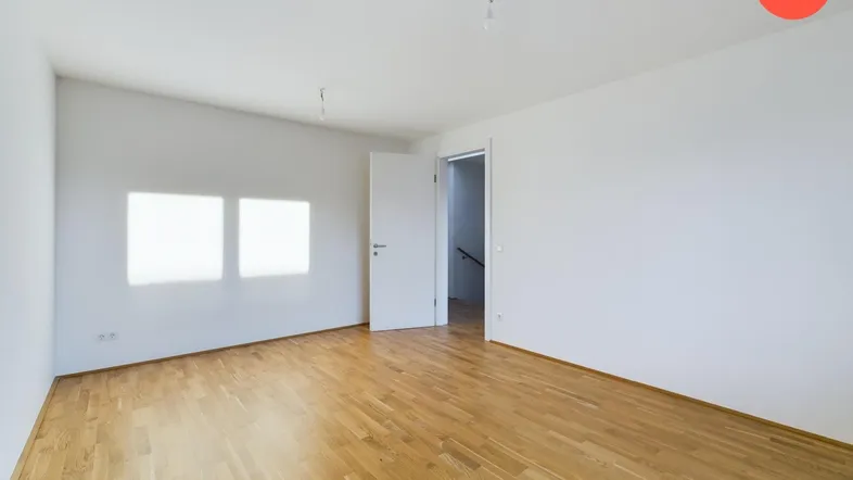 Helles, leeres Zimmer mit Parkettboden und zwei Fenstern, bereit zur individuellen Gestaltung.