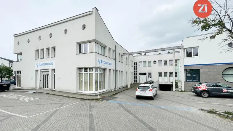 Gesamtansicht des modernen Gebäudekomplexes mit Geschäftsfassaden und umliegenden Parkplätzen.