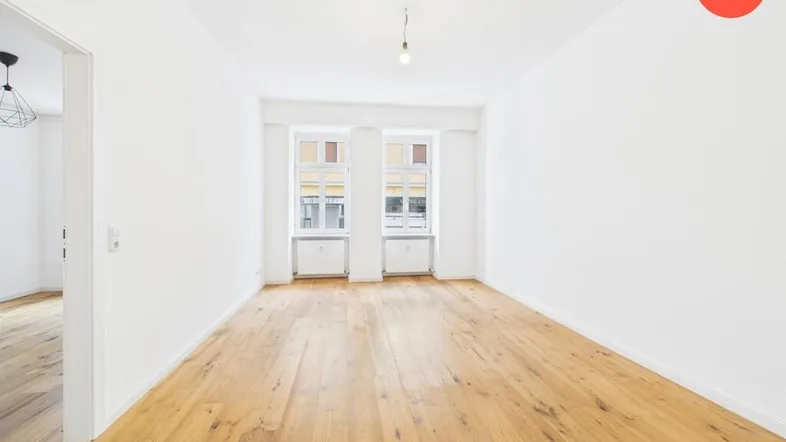 Helles und geräumiges Zimmer mit Holzboden und zwei großen Fenstern, ideal als Wohnbereich.