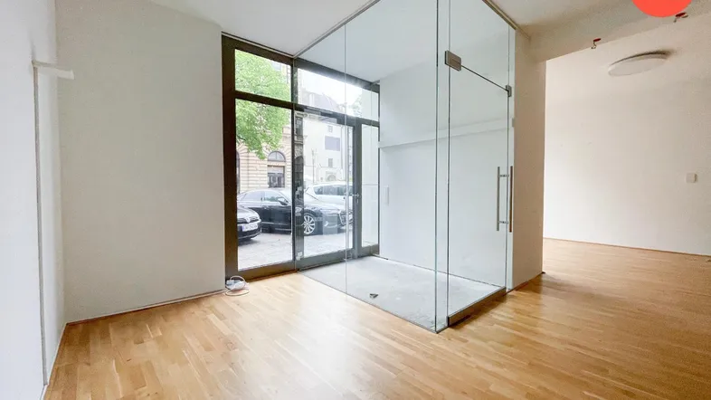 Heller, leerer Gewerberaum mit großen Fenstern zur Straße und einem modernen Glasbüro im Eingangsbereich.