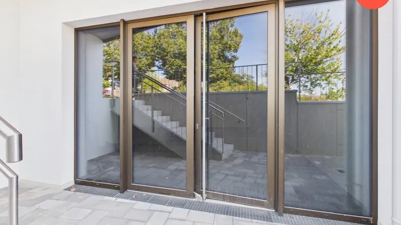 Eingangsbereich eines modernen Gebäudes mit großen Glasfronten und Außentreppe.