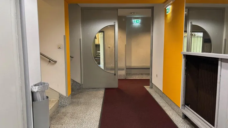 Eingangsbereich mit Terrazzoboden, gelben Akzentwänden und einer Tür mit runden Glaseinsätzen.