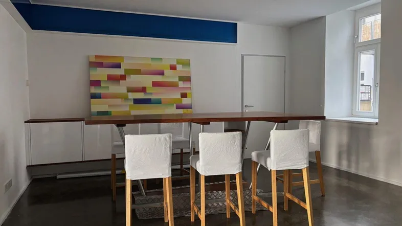 Geräumiger Essbereich mit langem Holztisch, modernen Stühlen und farbenfrohem Kunstwerk an der Wand.