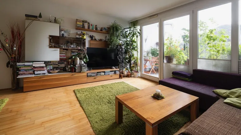 Helles Wohnzimmer mit Holzboden, vielen Pflanzen und Zugang zu einem Außenbereich.