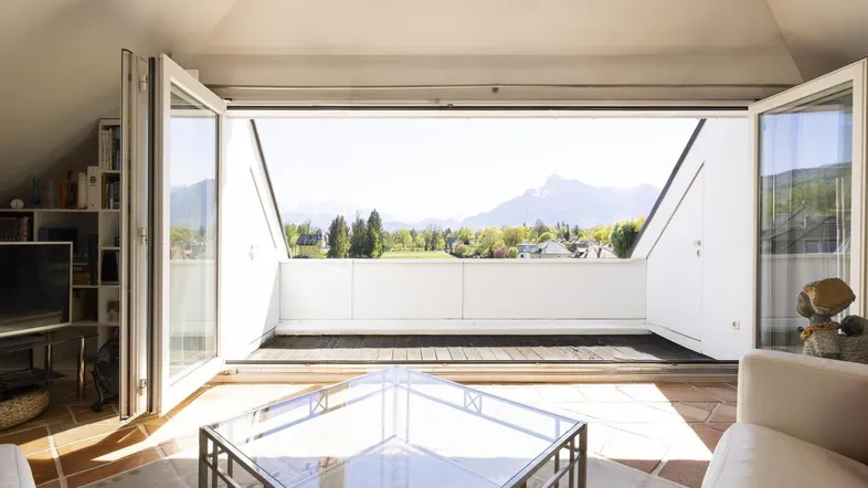 Helles Wohnzimmer im Dachgeschoss mit Zugang zu einem Balkon und weitem Bergblick.