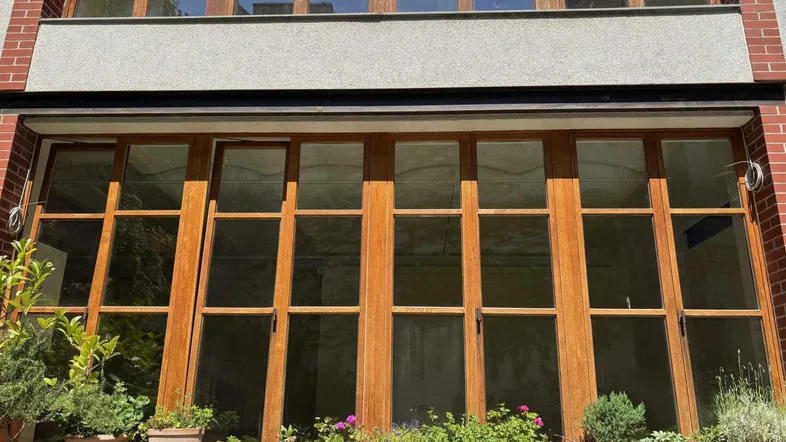 Fassade eines Gebäudes mit großen Holzfenstern und einer Reihe von Topfpflanzen auf der Fensterbank.