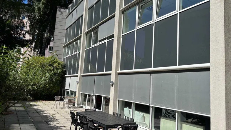 Große gepflasterte Terrasse mit Esstisch und Stühlen vor einem modernen Gebäude.