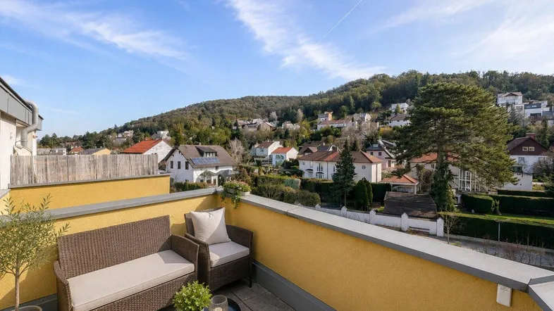 Sonniger Balkon mit bequemen Outdoor-Sitzmöbeln und weitem Blick über die grüne Umgebung.
