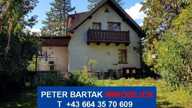 Traditionelles Haus mit Balkon und Garten umgeben von Bäumen unter blauem Himmel.