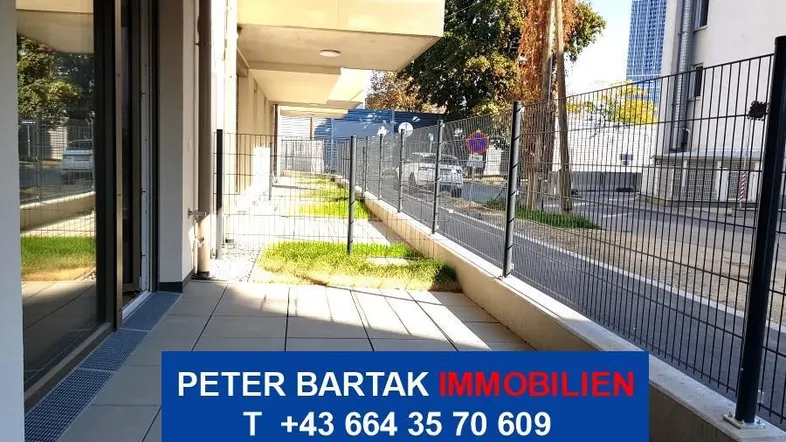 Gepflasterte Terrasse im Erdgeschoss mit Blick auf die Straße, umgeben von einem Zaun und Grünflächen.