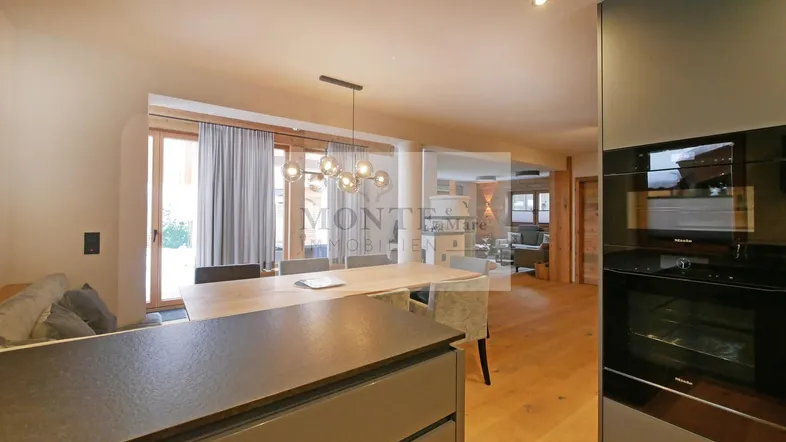 Heller Essbereich mit Holzboden und moderner Beleuchtung, angrenzend an die Küche mit Einbaugeräten.