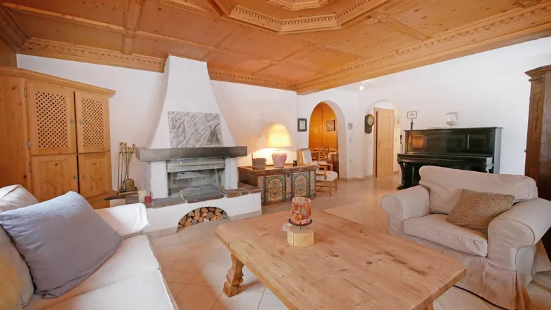 Gemütliches Wohnzimmer mit Holzkassettendecke, Kamin und Klavier, ideal für entspannte Abende.