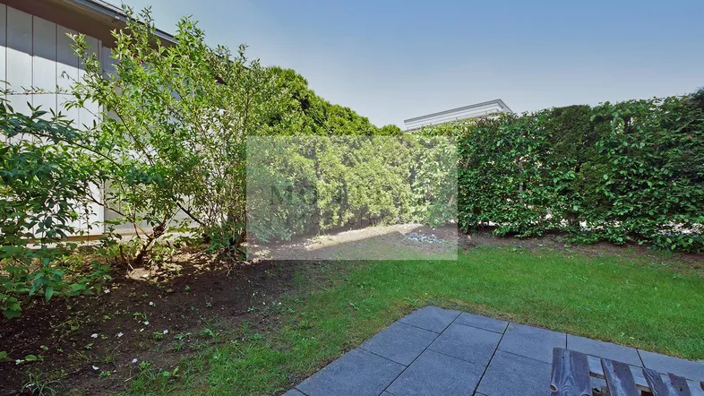 Gepflegter Gartenbereich mit Rasenfläche, Hecke und einer kleinen gepflasterten Terrasse.