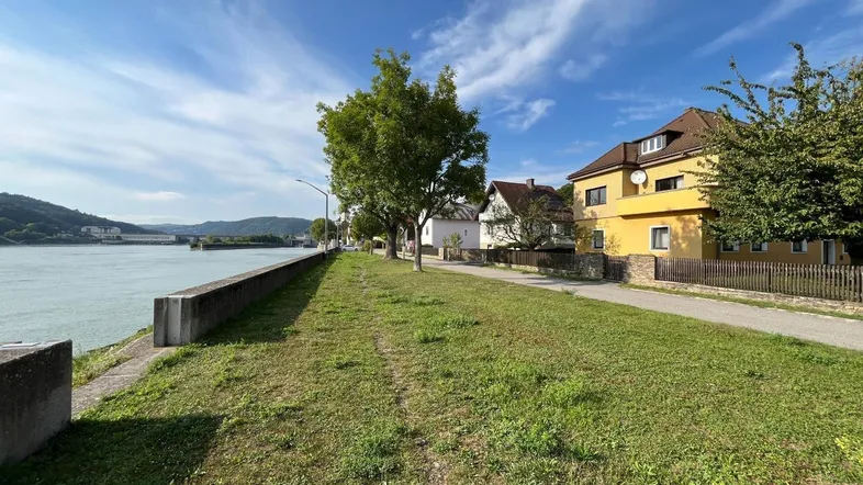 Panoramablick auf den Fluss mit dem gelben Haus und weiteren Gebäuden am Ufer.