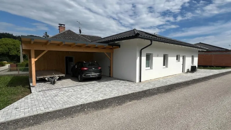 Modernes Einfamilienhaus mit Carport und gepflasterter Auffahrt unter bewölktem Himmel.