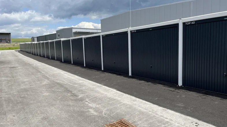 Lange Reihe von modernen, dunklen Garagentoren für Lagerzwecke unter bewölktem Himmel.