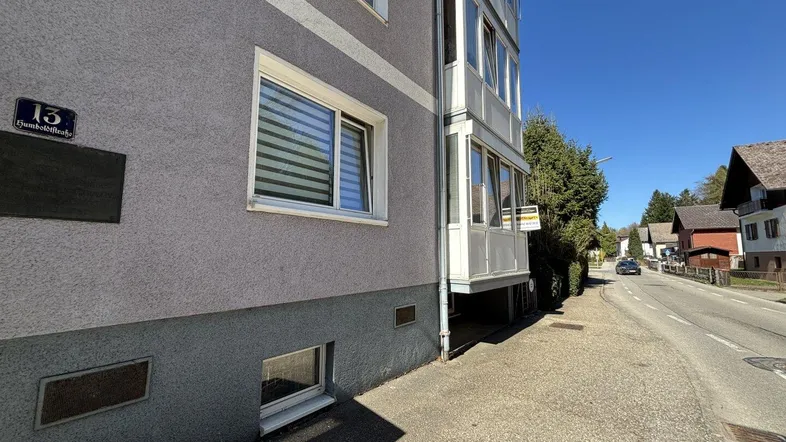 Graue Fassade eines Mehrfamilienhauses mit Balkonen und Blick auf die Straße an einem sonnigen Tag.