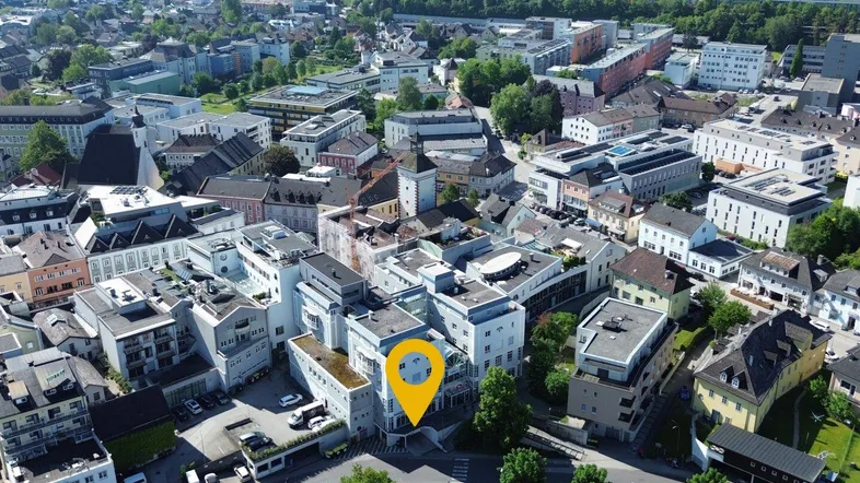 Luftaufnahme der Stadt mit dem markierten Gebäude und umliegender Bebauung in sonniger Umgebung.