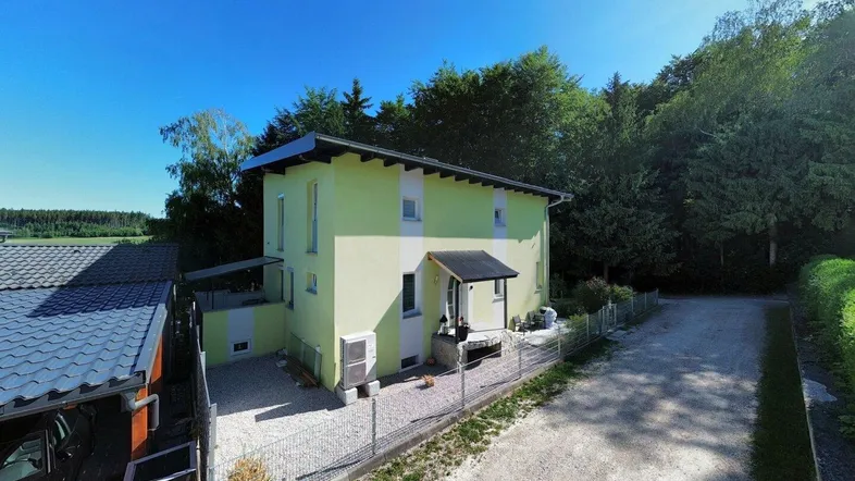 Freistehendes Einfamilienhaus mit heller Fassade, Schotterzufahrt und angrenzendem Carport.